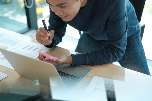 startup man writing reminder on sticky note. male freelancer student working organizing plan at workplace