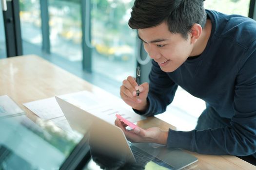 startup man writing reminder on sticky note. male freelancer student working organizing plan at workplace