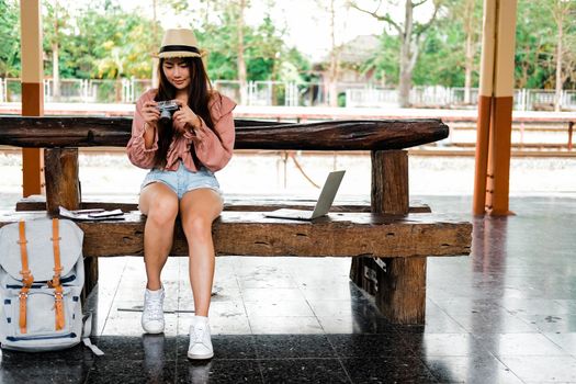 woman traveler holding camera taking photo at train station. travel trip journey concept