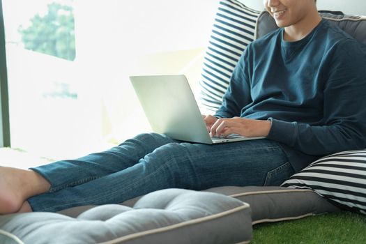 man sitting on floor in living room using computer at home. male teenager student studying doing assignment