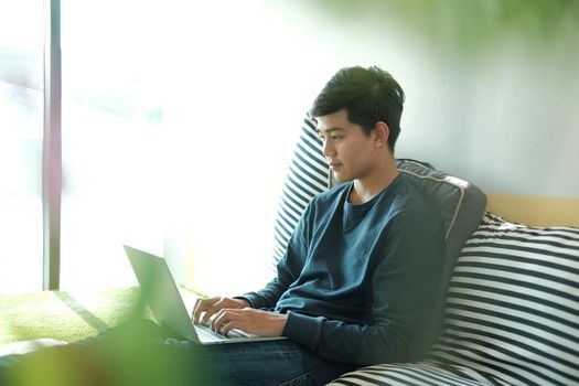 man sitting on floor in living room using computer at home. male teenager student studying doing assignment