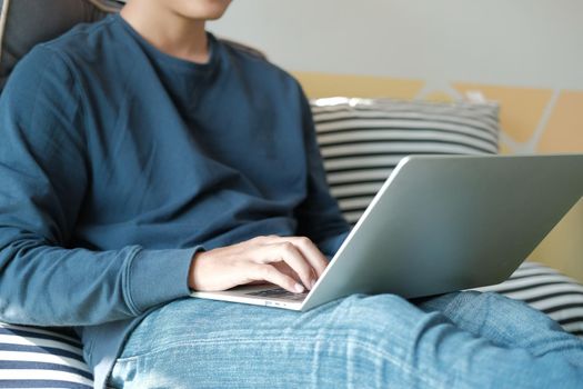 man sitting on floor in living room using computer at home. male teenager student studying doing assignment