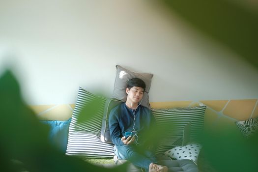 asian male teenager man listening to music from smart mobile phone while sitting on floor at home