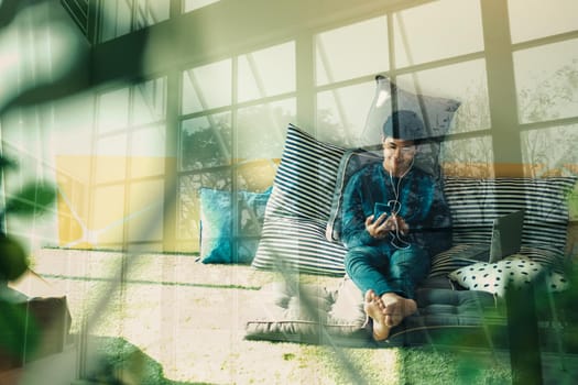 asian male teenager man listening to music from smart mobile phone while sitting on floor at home