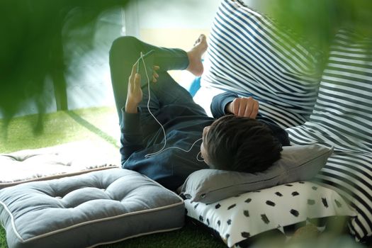 asian male teenager man listening to music from smart mobile phone while lying on floor at home