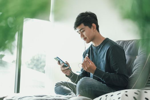 asian male teenager man listening to music from smart mobile phone while sitting on floor at home