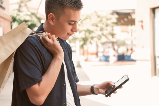 man holding paper shopping bags & using mobile smart phone. consumerism lifestyle