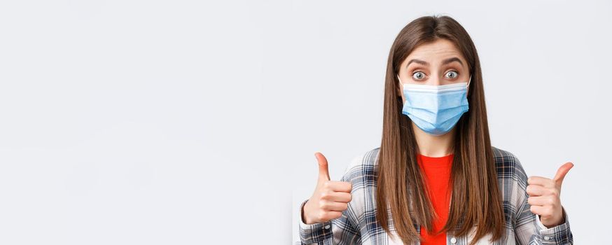 Coronavirus outbreak, leisure on quarantine, social distancing and emotions concept. Sounds good. Excited and pleased, satisfied female in medical mask, show thumb-up, interesting idea.