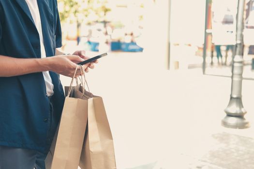 man holding paper shopping bags & using mobile smart phone. consumerism lifestyle