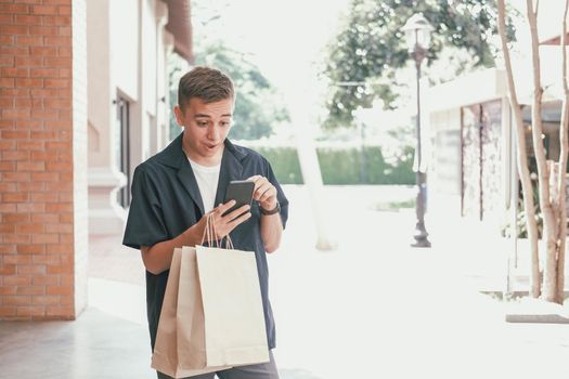 surprised man holding paper shopping bags & mobile smart phone. consumerism lifestyle