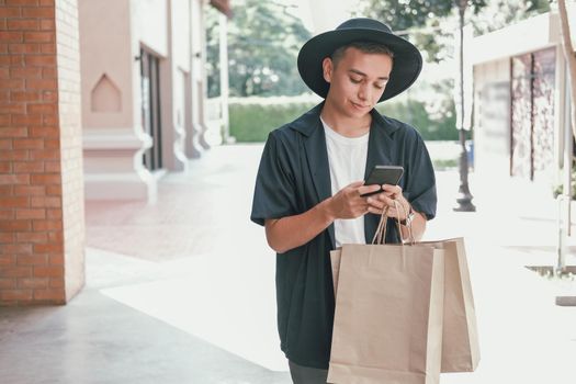 man holding paper shopping bags & using mobile smart phone. consumerism lifestyle