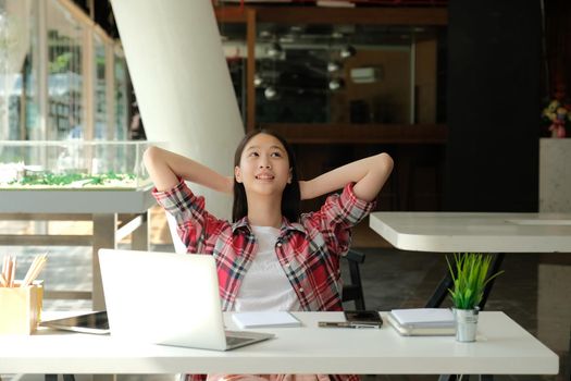 relaxed asian woman girl teenager keeping hands behind head relaxing resting at co-working space