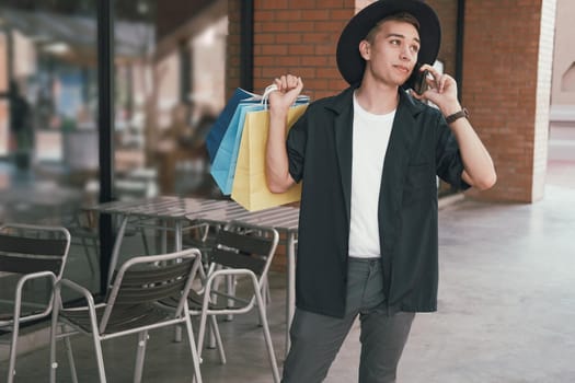 man holding paper shopping bags & talking on mobile smart phone. consumerism lifestyle