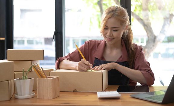 Starting Small business entrepreneur SME freelance,Portrait young woman working at home office, BOX,smartphone,laptop, online, marketing, packaging, delivery, SME, e-commerce concept.