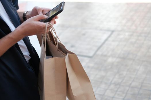 man holding paper shopping bags & using mobile smart phone. consumerism lifestyle