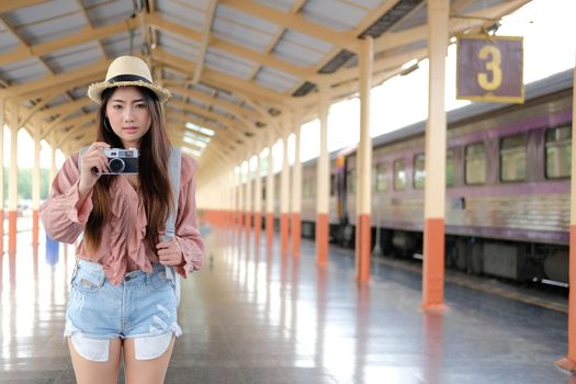 woman traveler holding camera taking photo at train station. travel trip journey concept