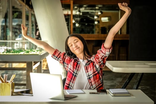 relaxed asian woman girl teenager stretching arms above head relaxing resting at co-working space