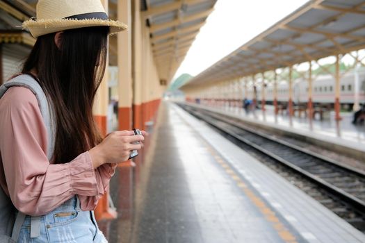 woman traveler holding camera taking photo at train station. travel trip journey concept