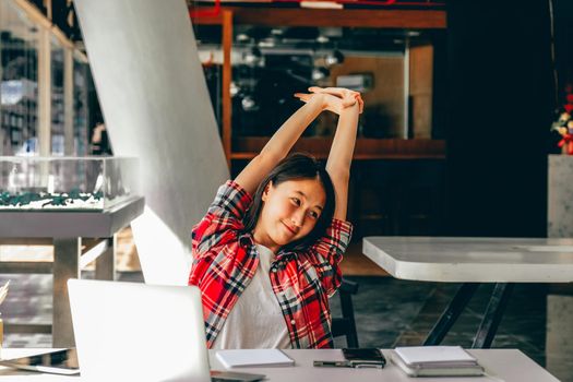 relaxed asian woman girl teenager stretching arms above head relaxing resting at co-working space