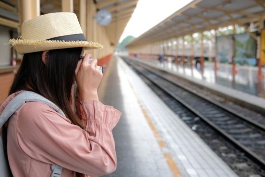 woman traveler holding camera taking photo at train station. travel trip journey concept