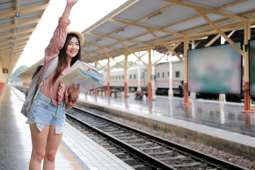 woman traveler with backpack map raising waving hand at train station. trip journey travel concept