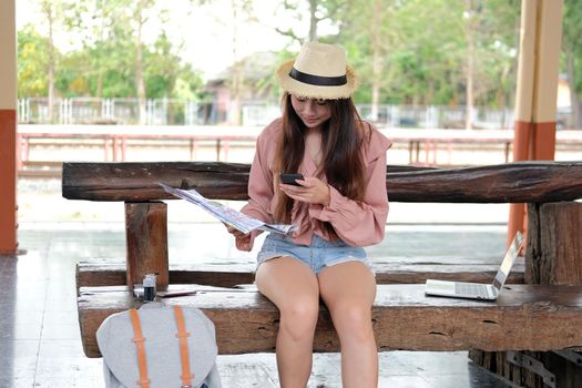 young woman traveler with mobile smart phone & map at train station. Travel journey trip concept