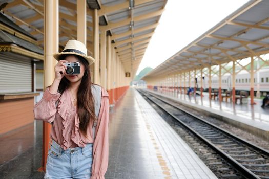 woman traveler holding camera taking photo at train station. travel trip journey concept