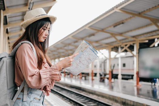 young asian woman backpacker traveler looking at map with backpack at train station while waiting for train. journey trip travel concept