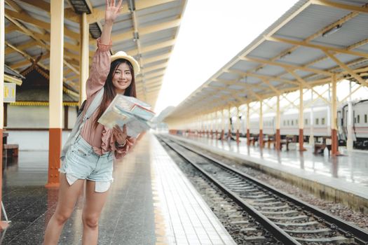 woman traveler with backpack map raising waving hand at train station. trip journey travel concept