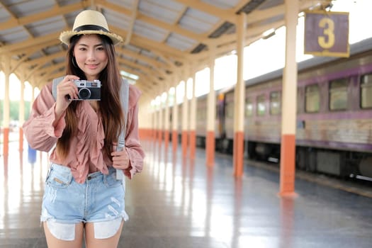 woman traveler holding camera taking photo at train station. travel trip journey concept