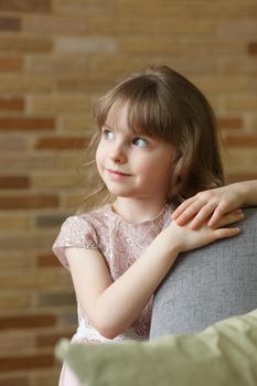 Adorable little girl looking at camera at home, smiling preschool pretty child with beautiful happy face posing alone on sofa, cute positive cheerful kid headshot portrait