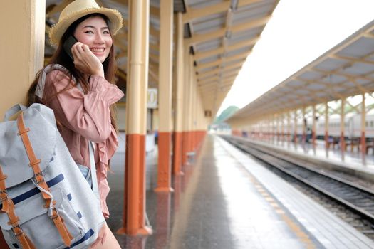 woman traveler with backpack talking on mobile smart phone at train station. trip journey travel concept