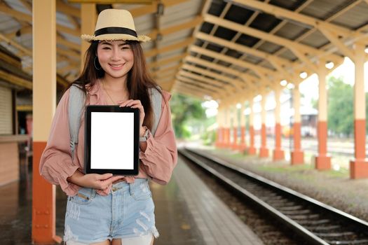 young woman traveler showing tablet with blank screen at train station. Travel journey trip concept