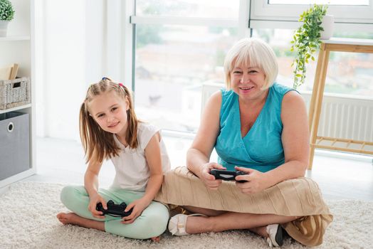 Smiling grandmother playing on console with granddaughter at home