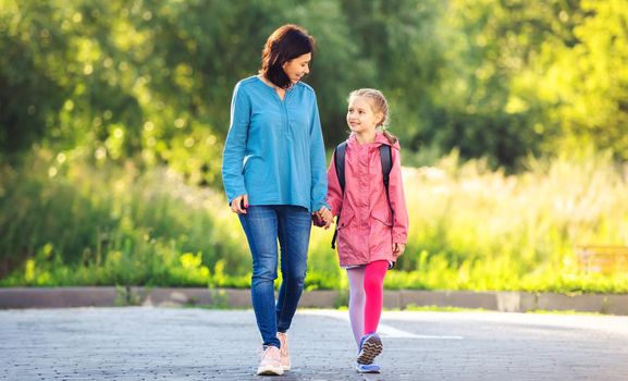 Little girl going to school with mother holding hand and smiling on sunny nature background