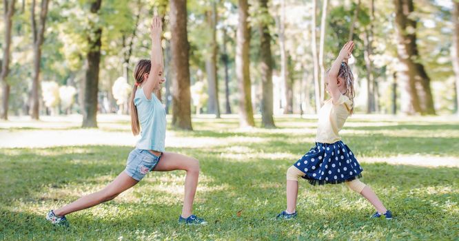 Two girls exercising together on green grass in park in beautiful sunny day