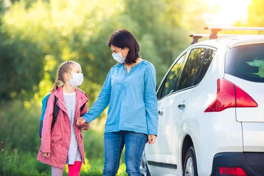 Little girl going back to school with mother through car parking during coronavirus pandemic