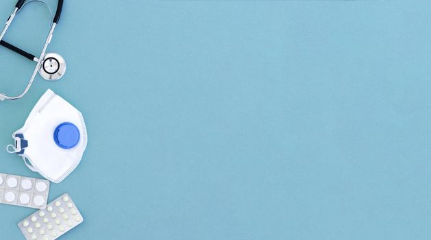 Pills in blisters, medical mask, phonendoscope, puzzle pieces on blue with copy space, top view