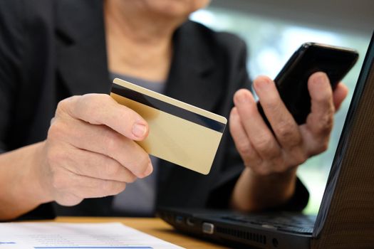 woman holding credit card using smart phone for online shopping. businesswoman purchase product from internet, make payment on bank website at workplace