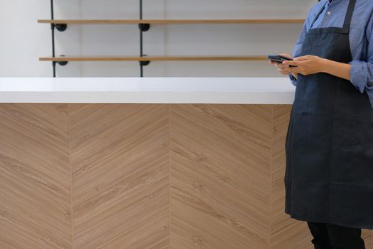 business owner wearing apron holding mobile phone at counter bar. man using smartphone at cafe coffee shop cafeteria restaurant