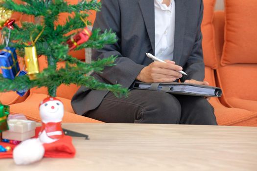 woman wearing suit holding notebook with gift present box christmas tree on table. xmas new year celebration.