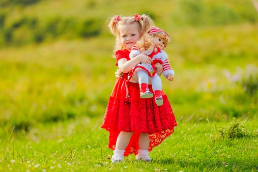 girl in a red dress and with a doll in her hands stands in nature