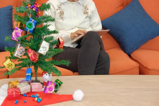 woman sitting on sofa using tablet at home. girl texting message on touchpad during xmas. christmas holiday new year celebration season greetings