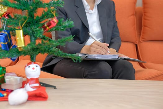 woman wearing suit writing note on notebook with gift present box christmas tree on table. xmas new year celebration.