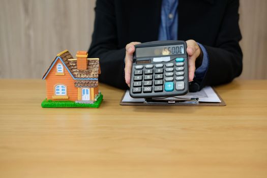 realtor agent with house model showing calculated price number on calculator. buying renting property. real estate insurance.