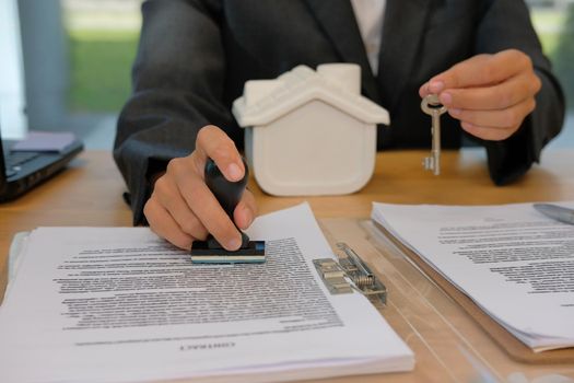 real estate agent with house key using stamper for stamping approved on mortgage loan contract agreement document