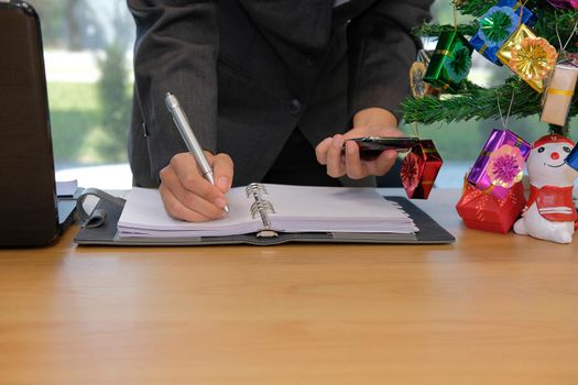 man writing reminder schedule note on notebook. businessman working organizing plan with smart phone at workplace office during christmas new year holiday