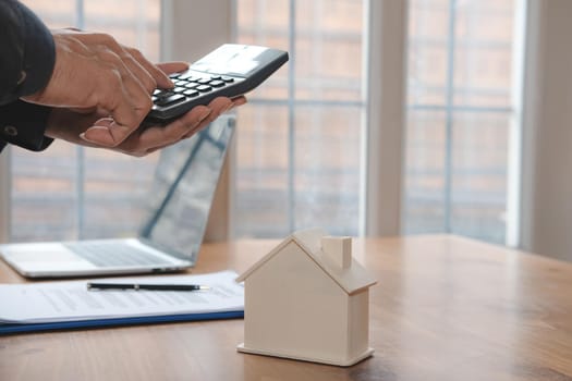businessman using calculator to calculate invoice with house model. mortgage, real estate & property concept