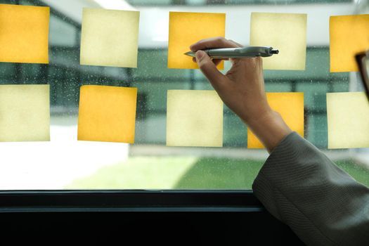 Businessman write on adhesive notes on glass wall at workplace. Sticky note paper reminder schedule for discussing creative idea & business brainstorming