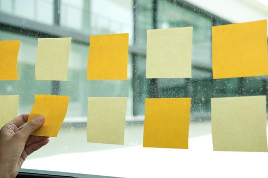 hand hold adhesive notes on glass wall at workplace. Sticky note paper reminder schedule for creative idea & business brainstorming